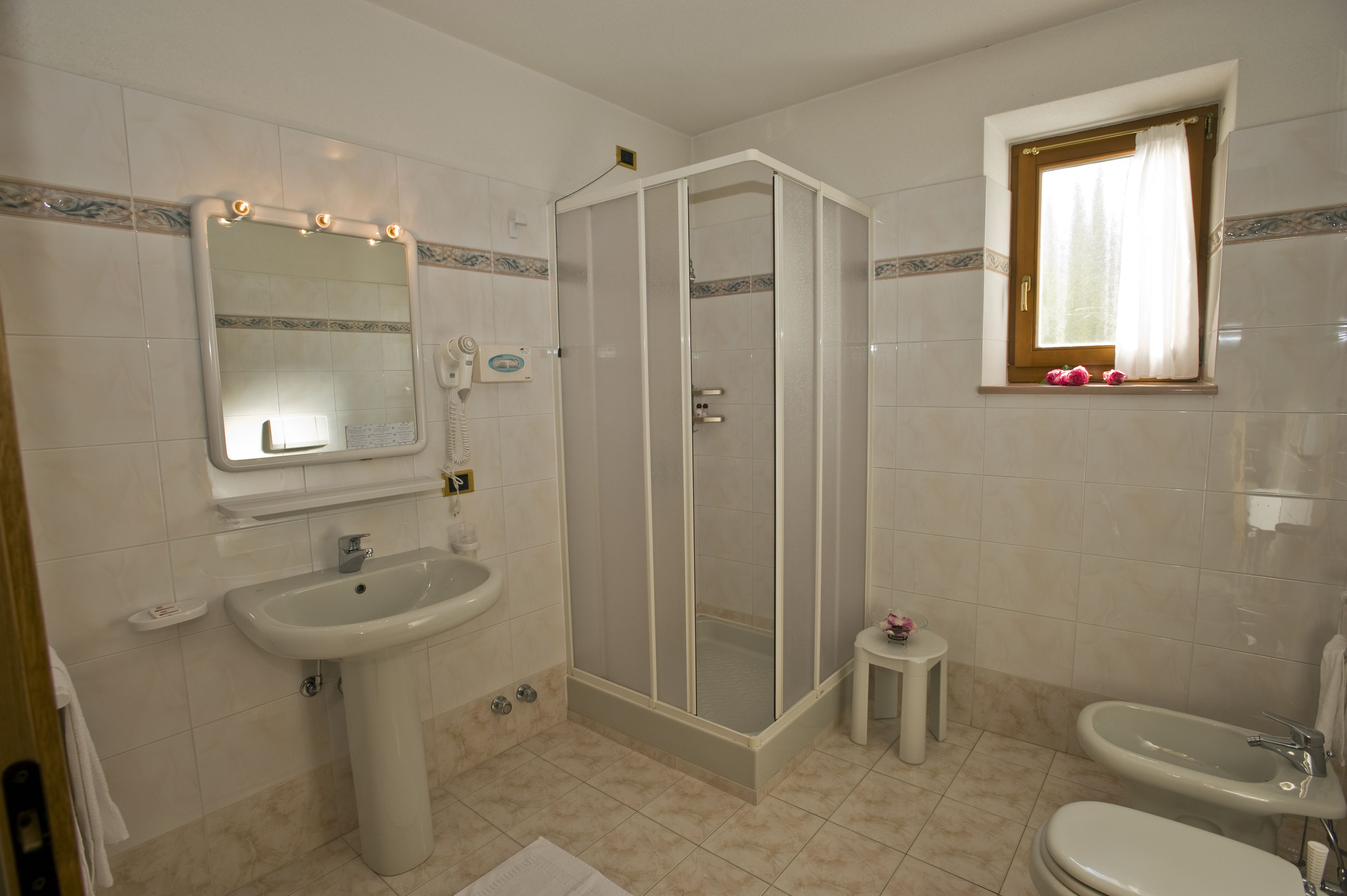 A bathroom with a sink, mirror, shower enclosure, toilet, and a window with a curtain.