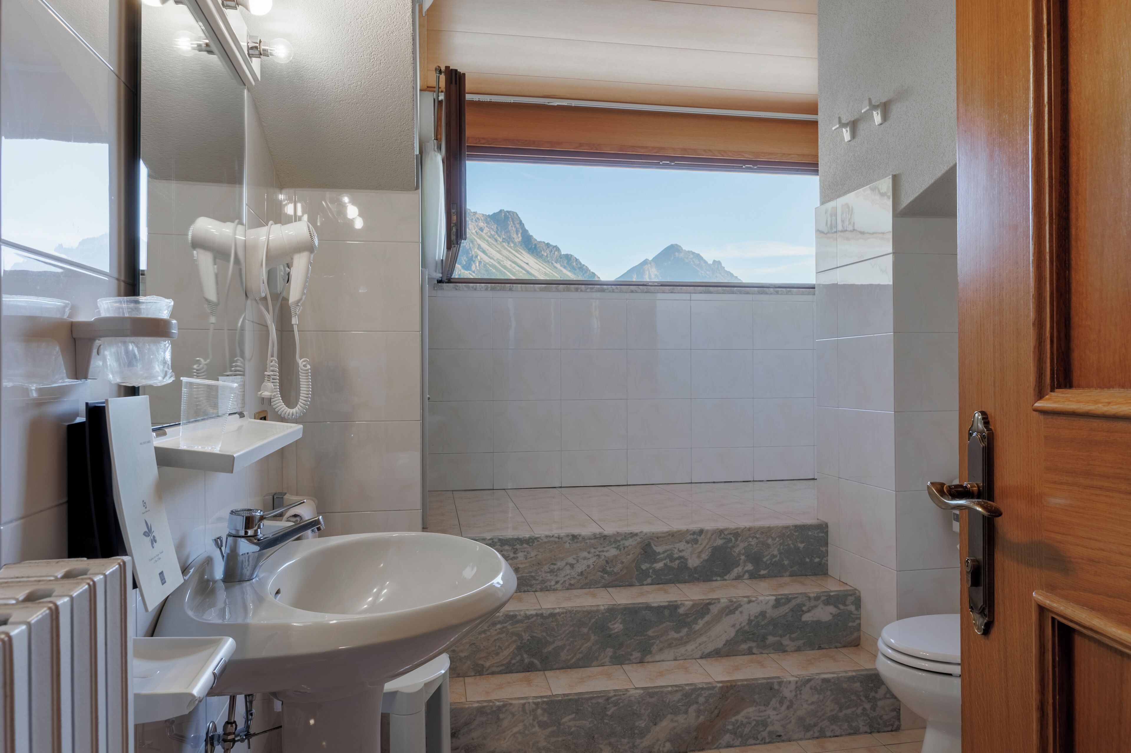 Baño con lavamanos, espejo, secador de pelo y vistas a las montañas a través de una ventana.