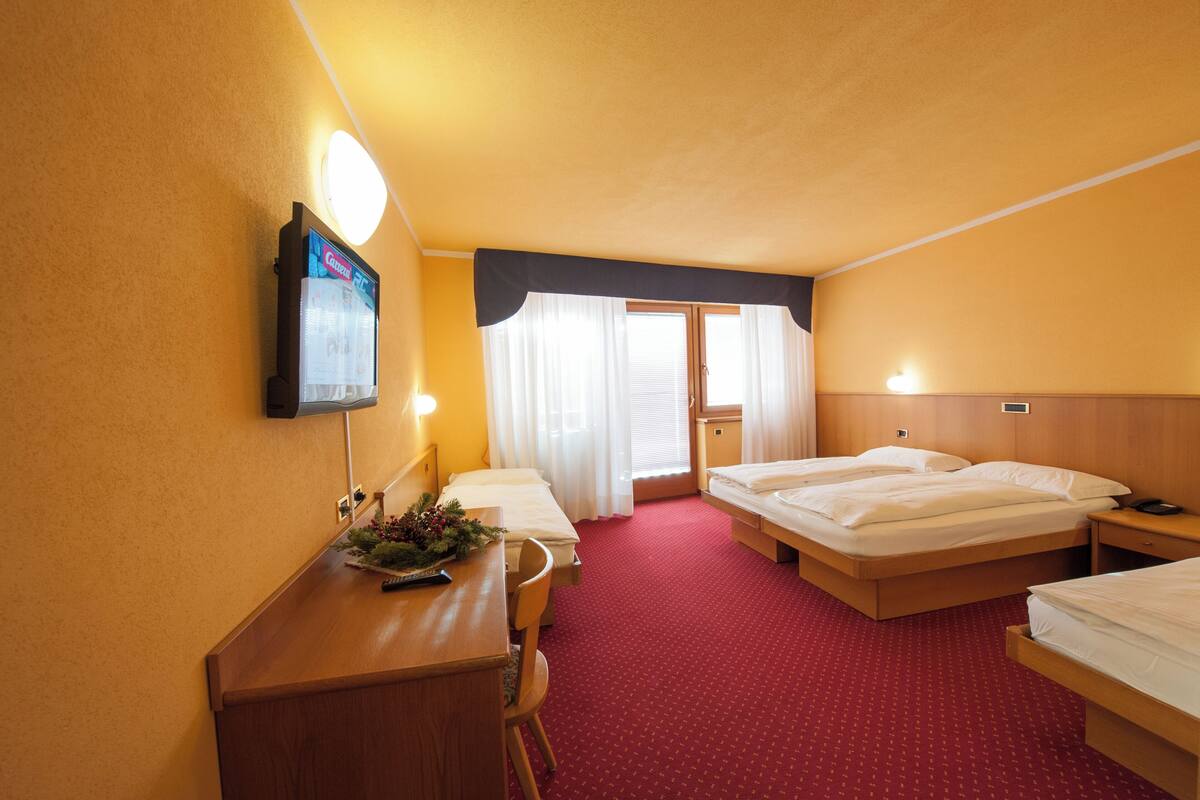 Habitación de hotel con dos camas, un escritorio, una silla, un televisor y una ventana con cortinas.