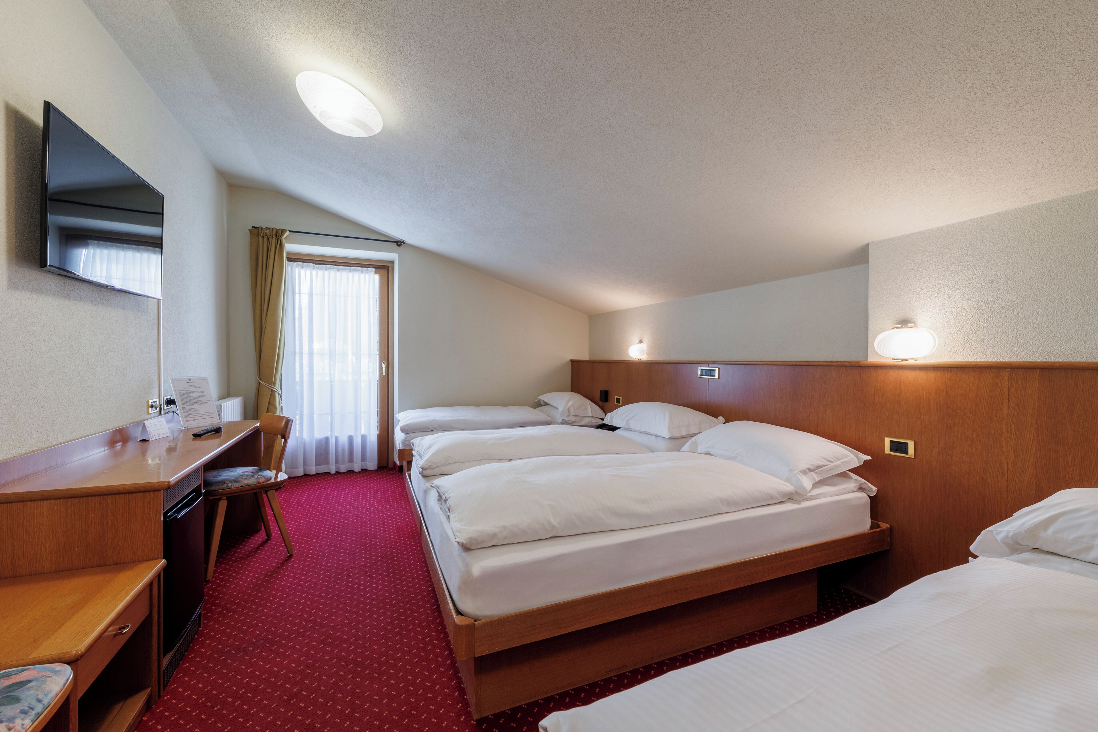 A hotel room with a desk, two beds, a TV, and a window with curtains.