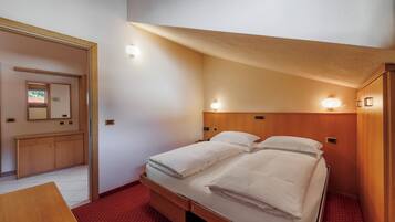 Et lille hotelværelse med en enkeltseng, et træskab, et skrivebord og et spejl på væggen.