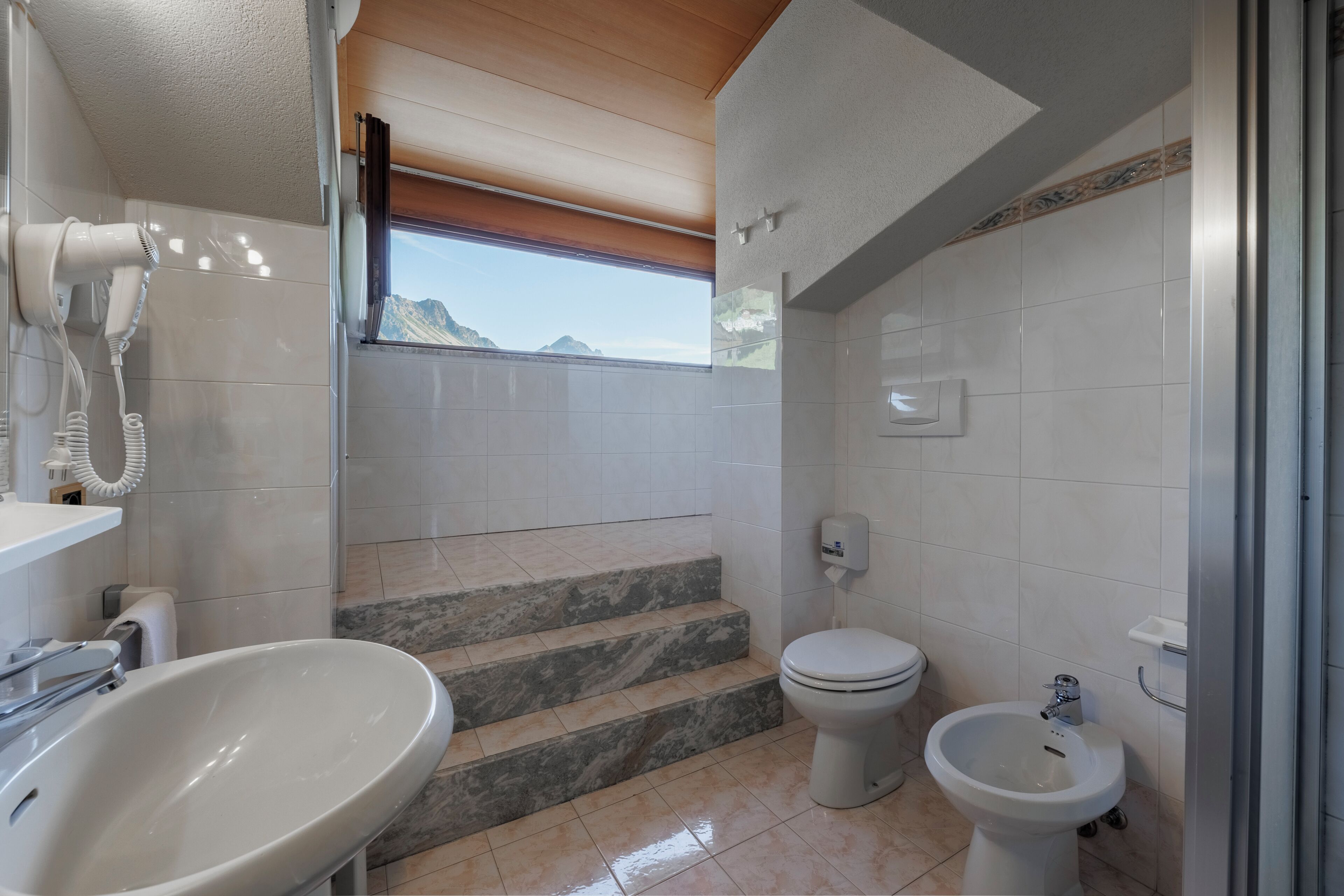 Une salle de bain équipée d’un lavabo, de toilettes, d’un bidet et d’un sèche-cheveux fixé au mur.