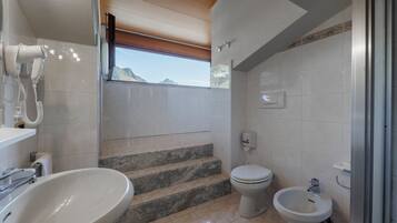 Une salle de bain équipée d’un lavabo, de toilettes, d’un bidet et d’un sèche-cheveux fixé au mur.