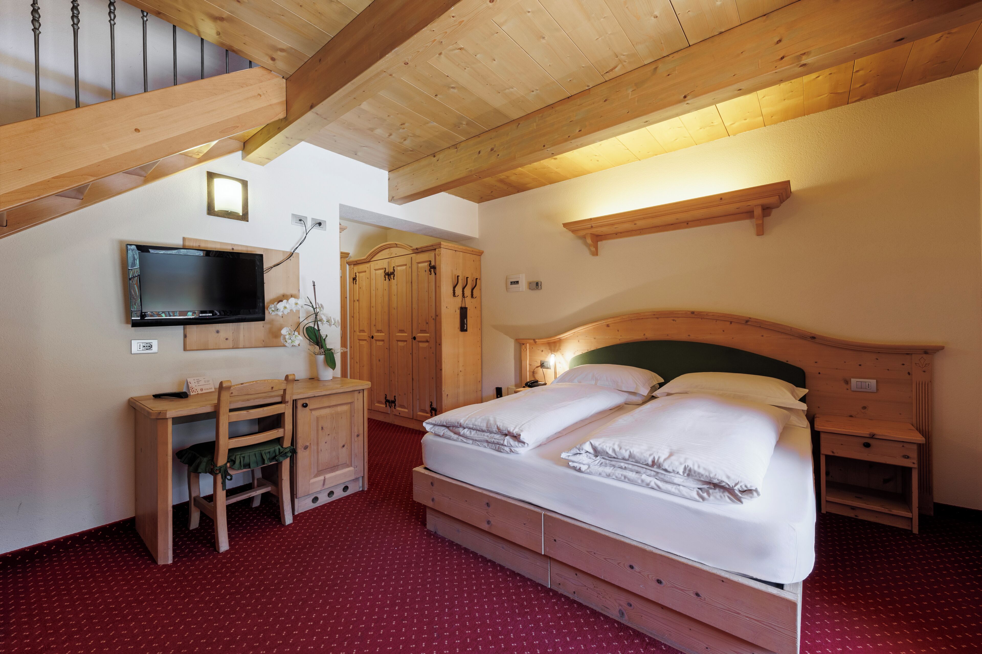A bedroom with a bed, wooden desk, television, and wardrobe.