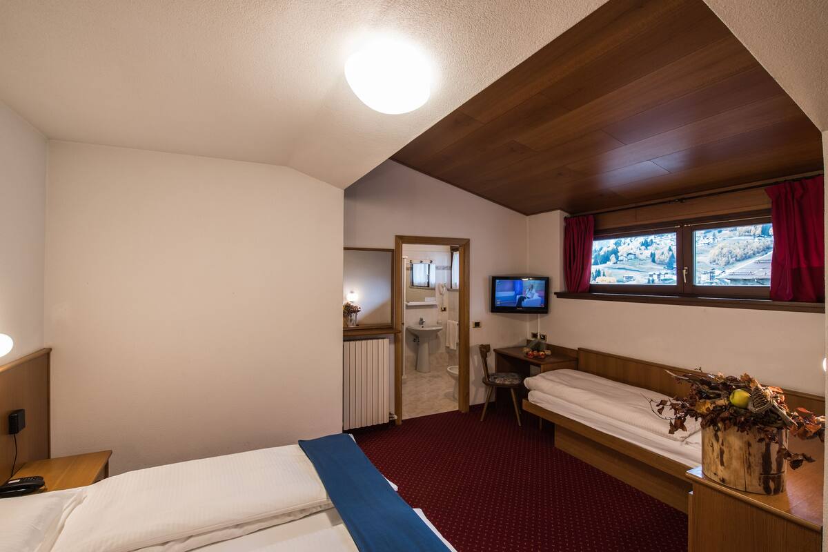 Habitación de hotel con dos camas, un televisor, una ventana que ofrece vistas a un paisaje nevado y un baño visible a través de una puerta abierta.