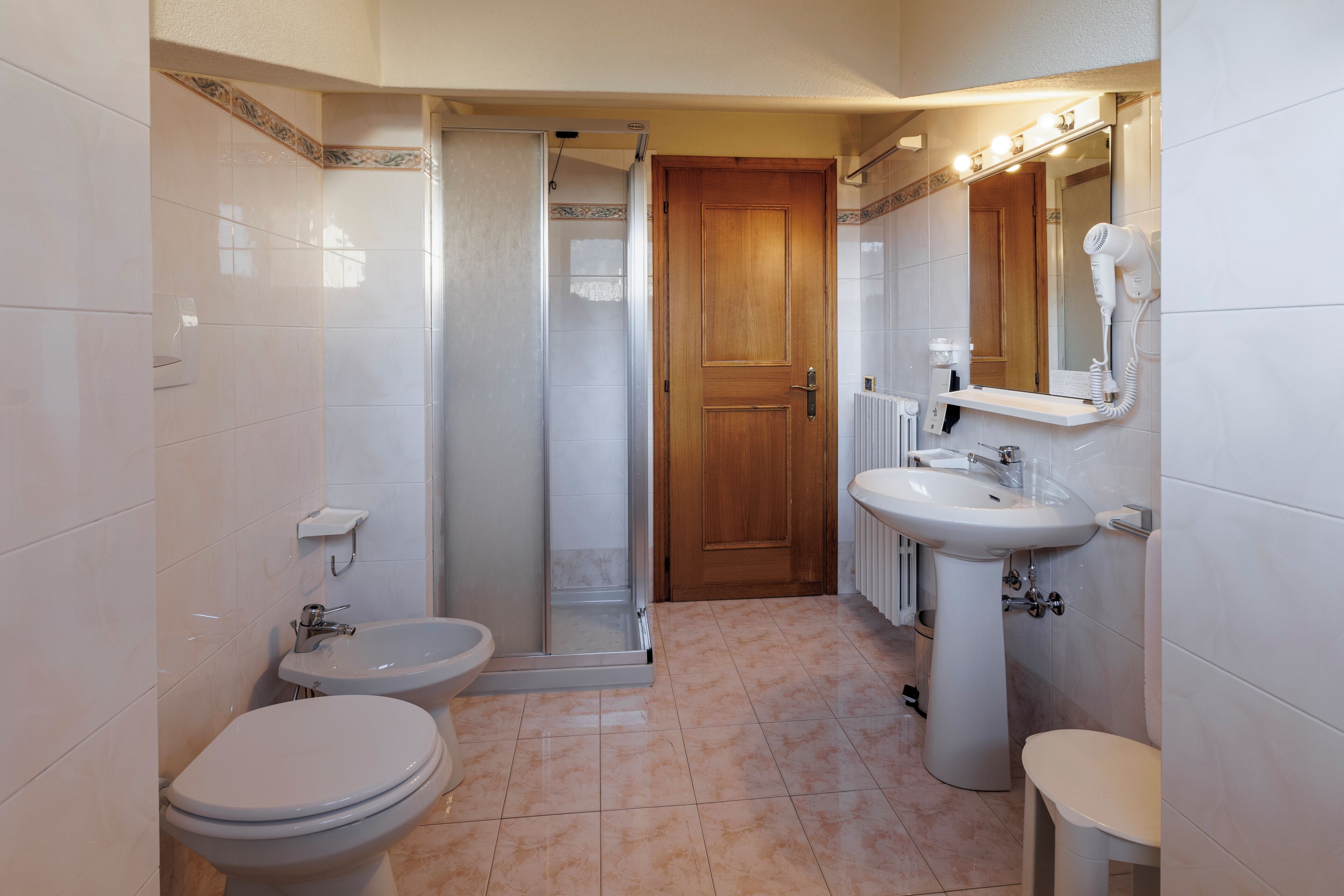 Une salle de bain équipée d’une douche, de toilettes, d’un bidet, d’un lavabo et d’un miroir.