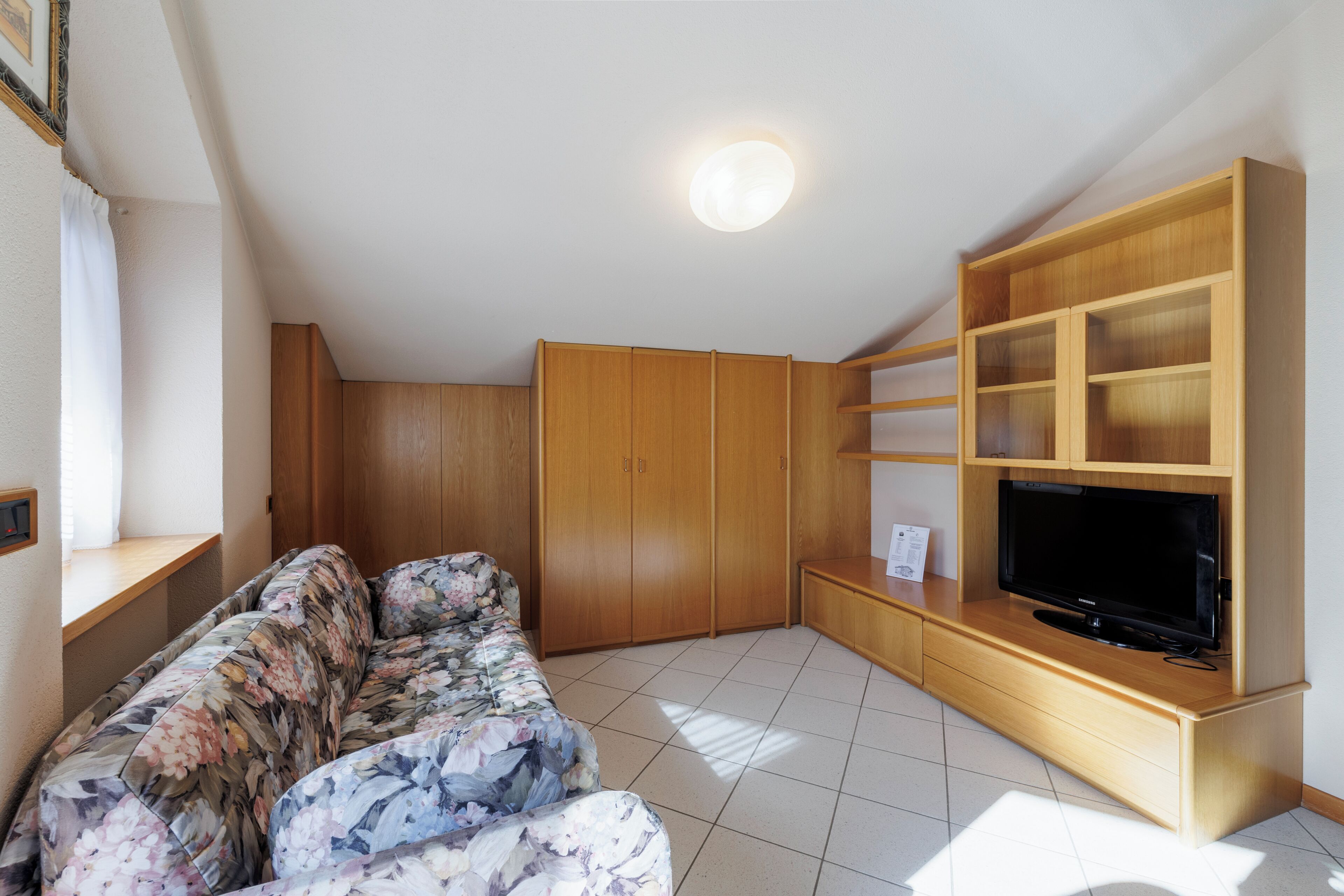A living room with a sofa, wooden wardrobe, TV stand, and a ceiling light.