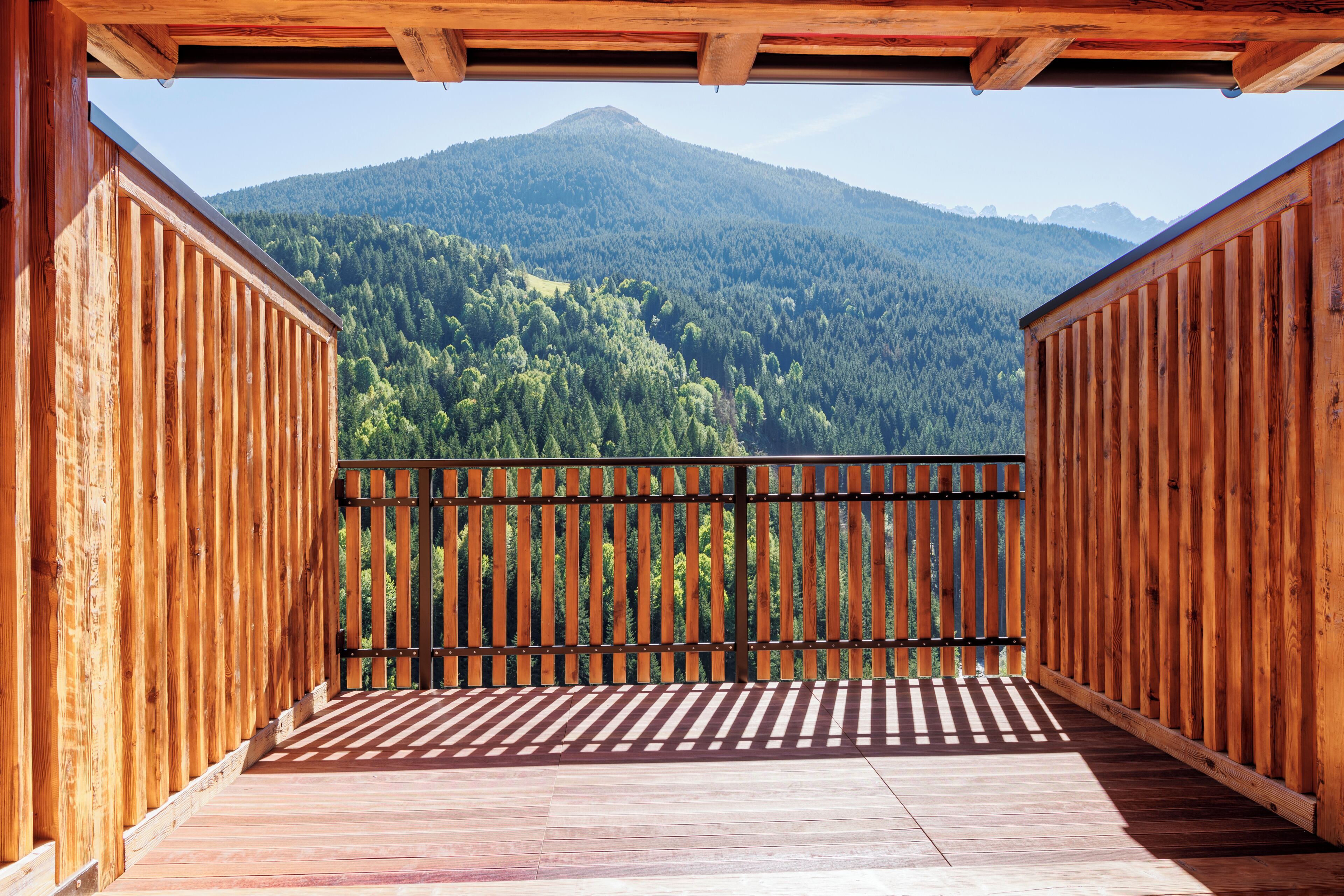 A wooden balcony with a view of a forested mountain.