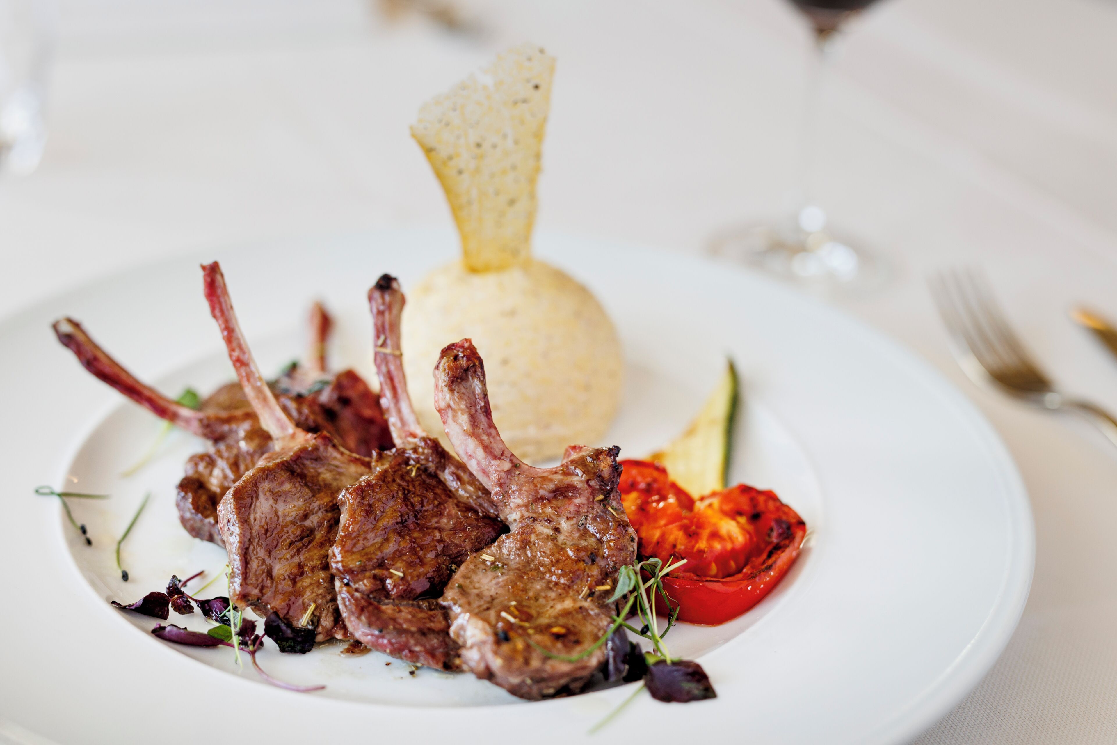 A plate of food with lamb chops, a tomato, and a small mound of what appears to be mashed potatoes.