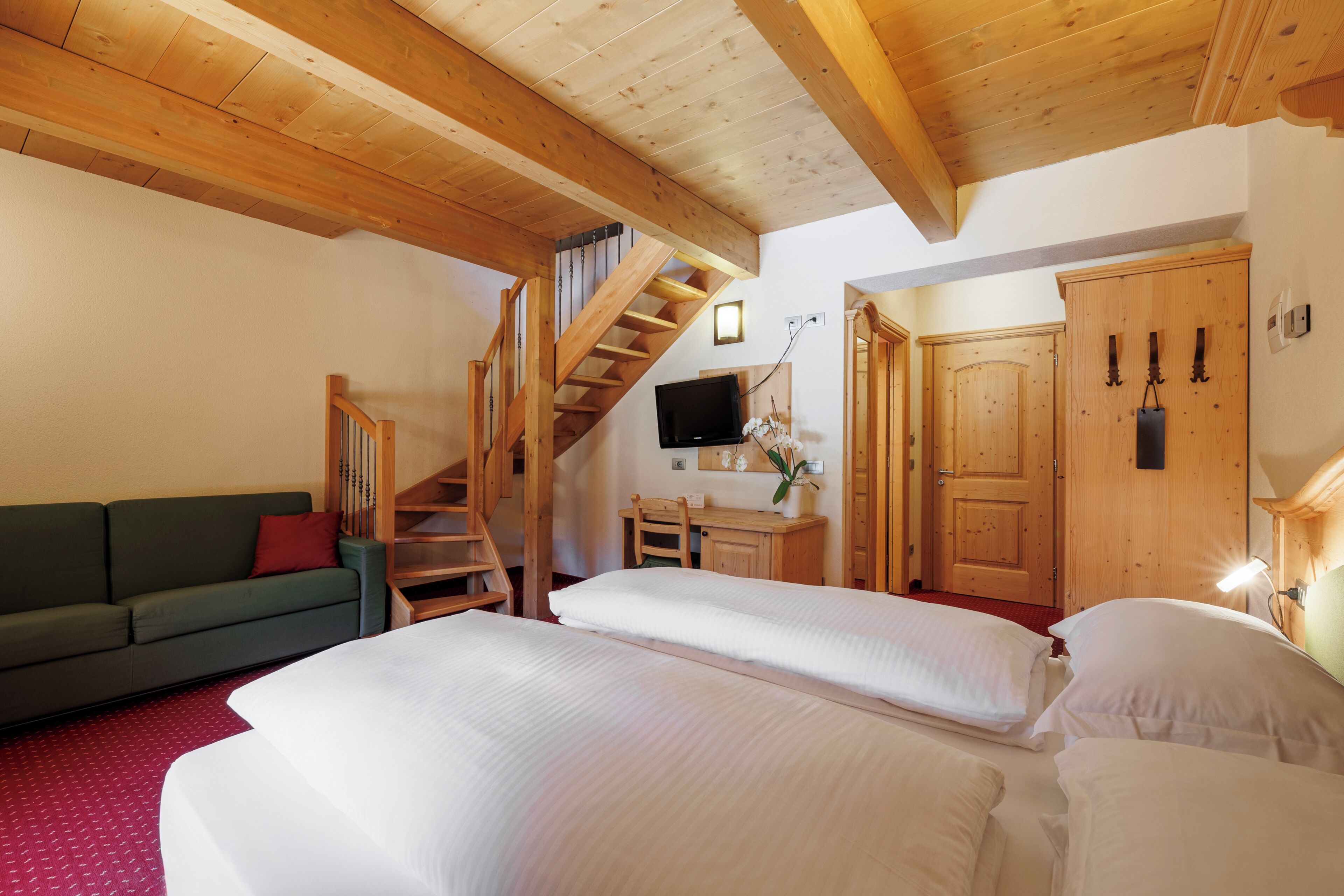 A room with wooden beams, a staircase, a bed, a desk, a television, and a wardrobe.