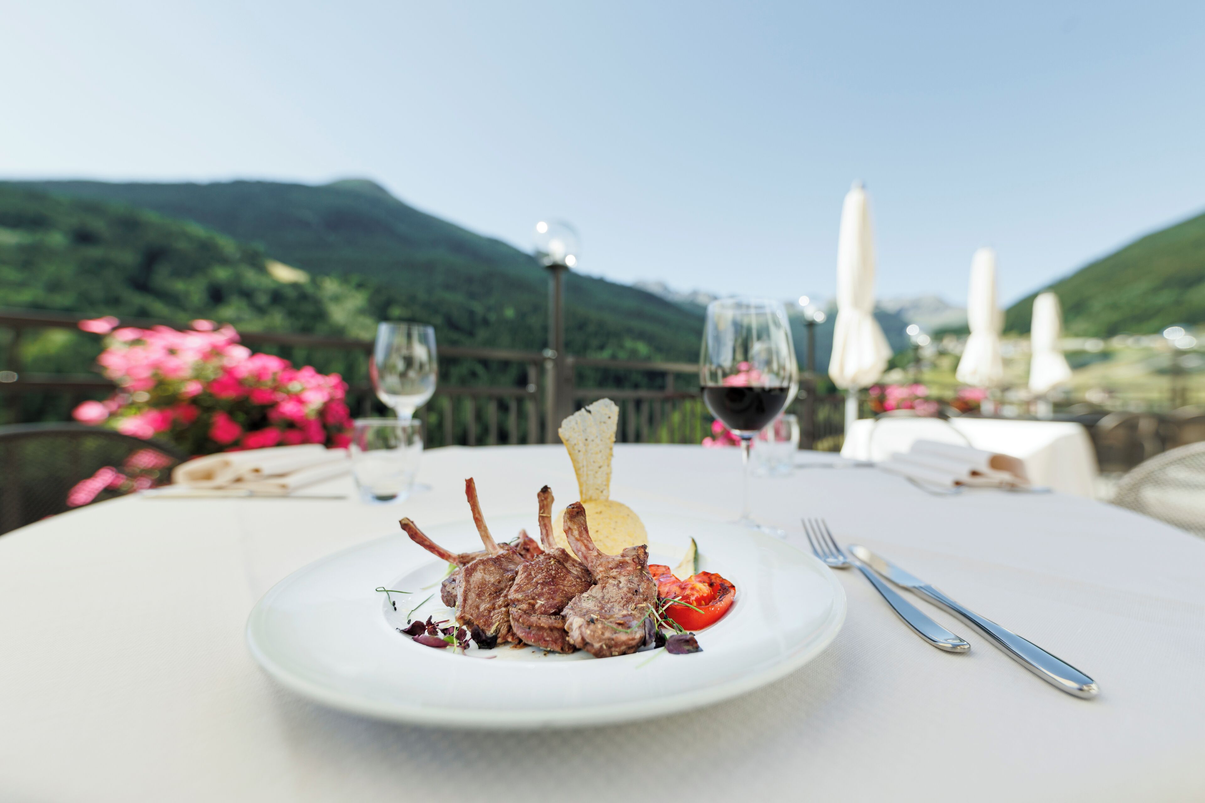 A dining table with a plate of food, cutlery, and a glass of red wine.