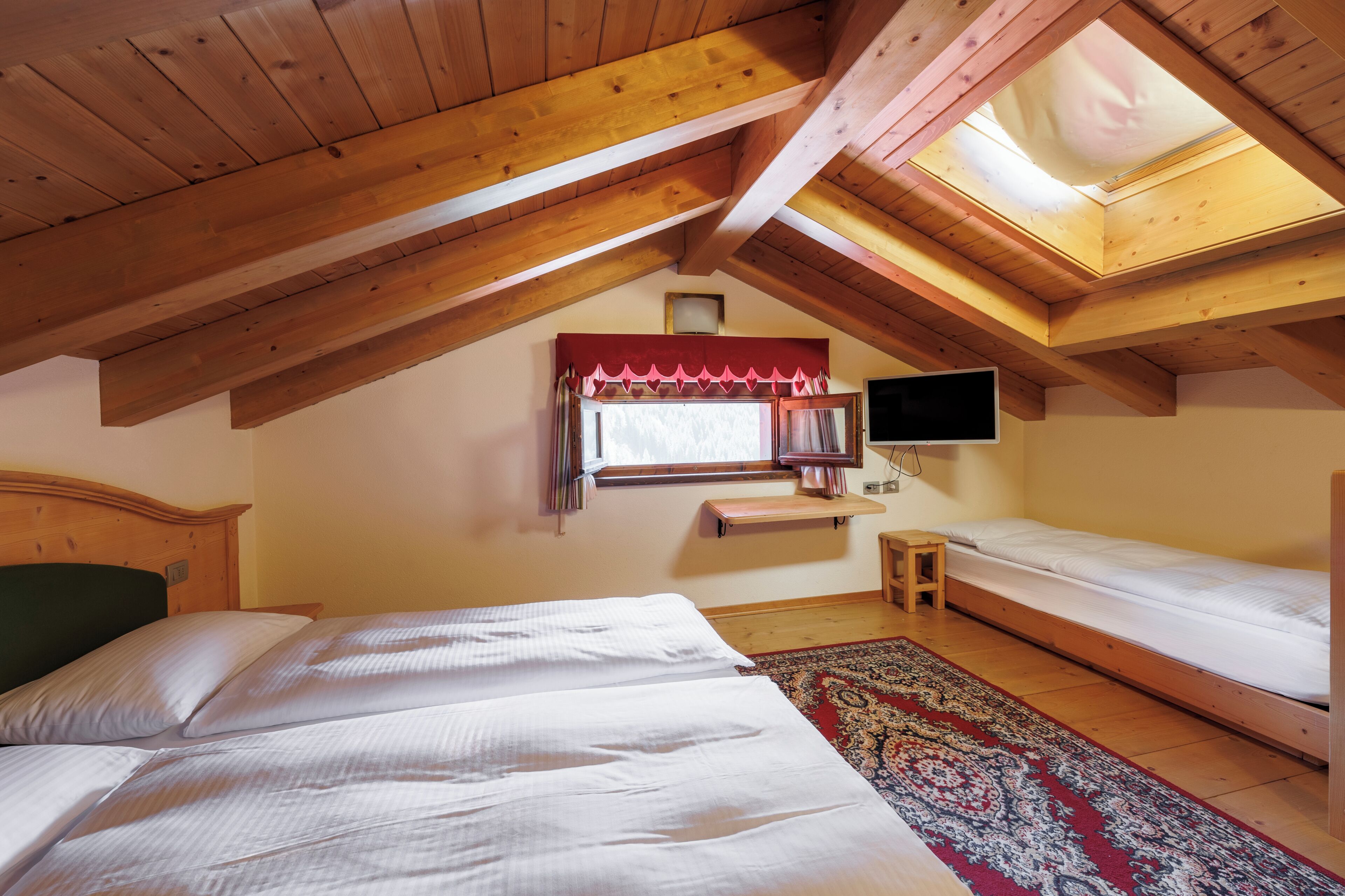 A room with two beds, a television, a window with curtains, and a skylight.