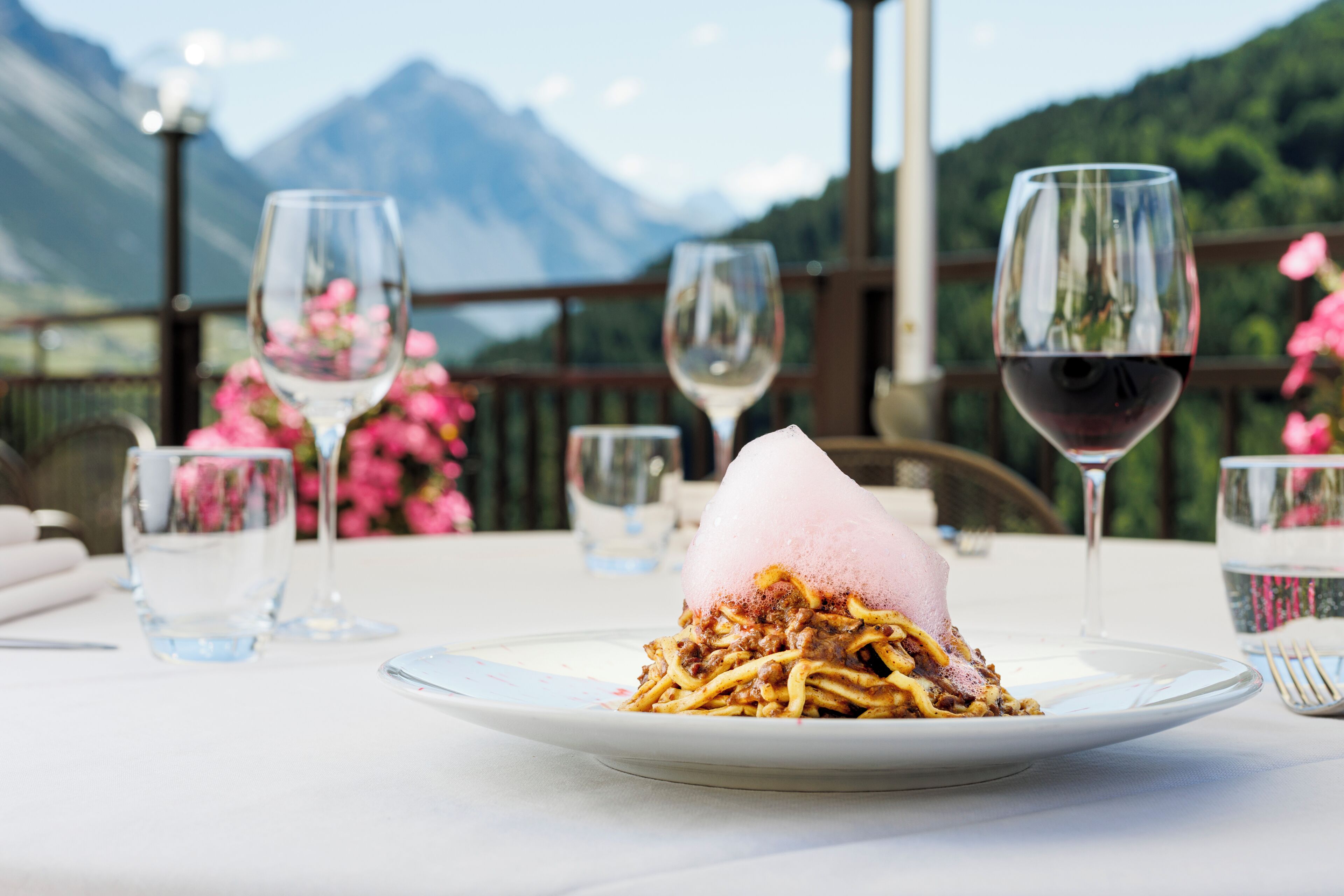 A dining table with a plate of food, glasses, and a mountain view in the background.