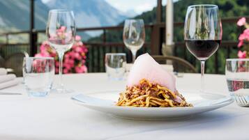 A dining table with a plate of food, glasses, and a mountain view in the background.