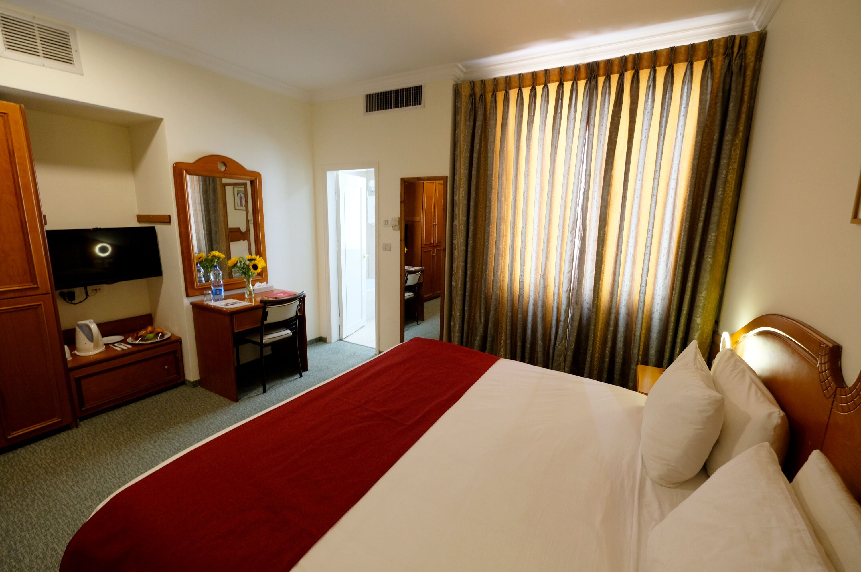 A hotel room with a large bed, a desk with a chair, a television, and a wardrobe.