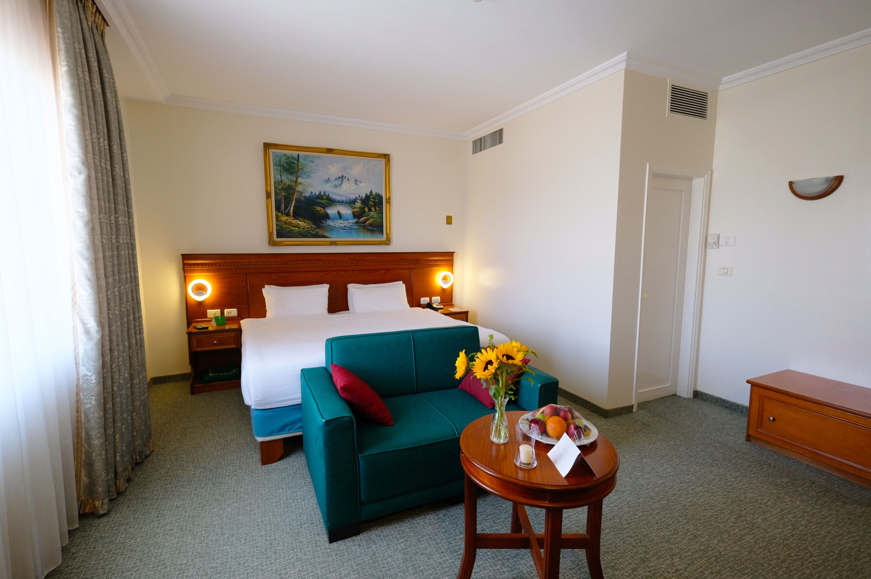Ein Hotelzimmer mit einem Bett, einem grünen Sofa, einem kleinen Tisch mit Blumenvase und einem Bild an der Wand.