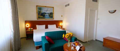 Ein Hotelzimmer mit einem Bett, einem grünen Sofa, einem kleinen Tisch mit Blumenvase und einem Bild an der Wand.