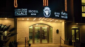 The entrance of City Inn Palace Hotel with a sign in multiple languages, a glass door entrance, and a security rope barrier. - City Inn Palace Hotel (Ramallah)