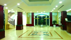 A hotel lobby with a central reception desk, a staircase, and a large potted plant. - City Inn Palace Hotel (Ramallah)