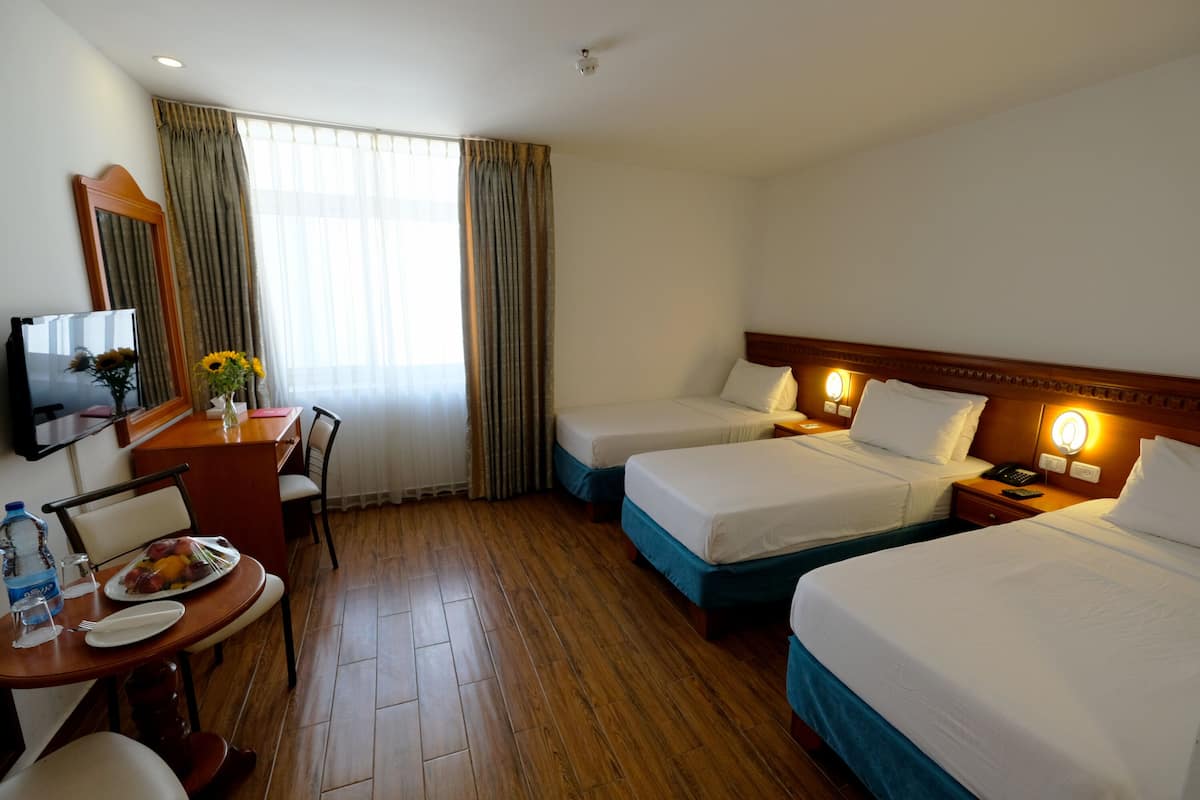 A hotel room with two beds, a desk with a chair, a TV, and a dining area with a table and chairs.