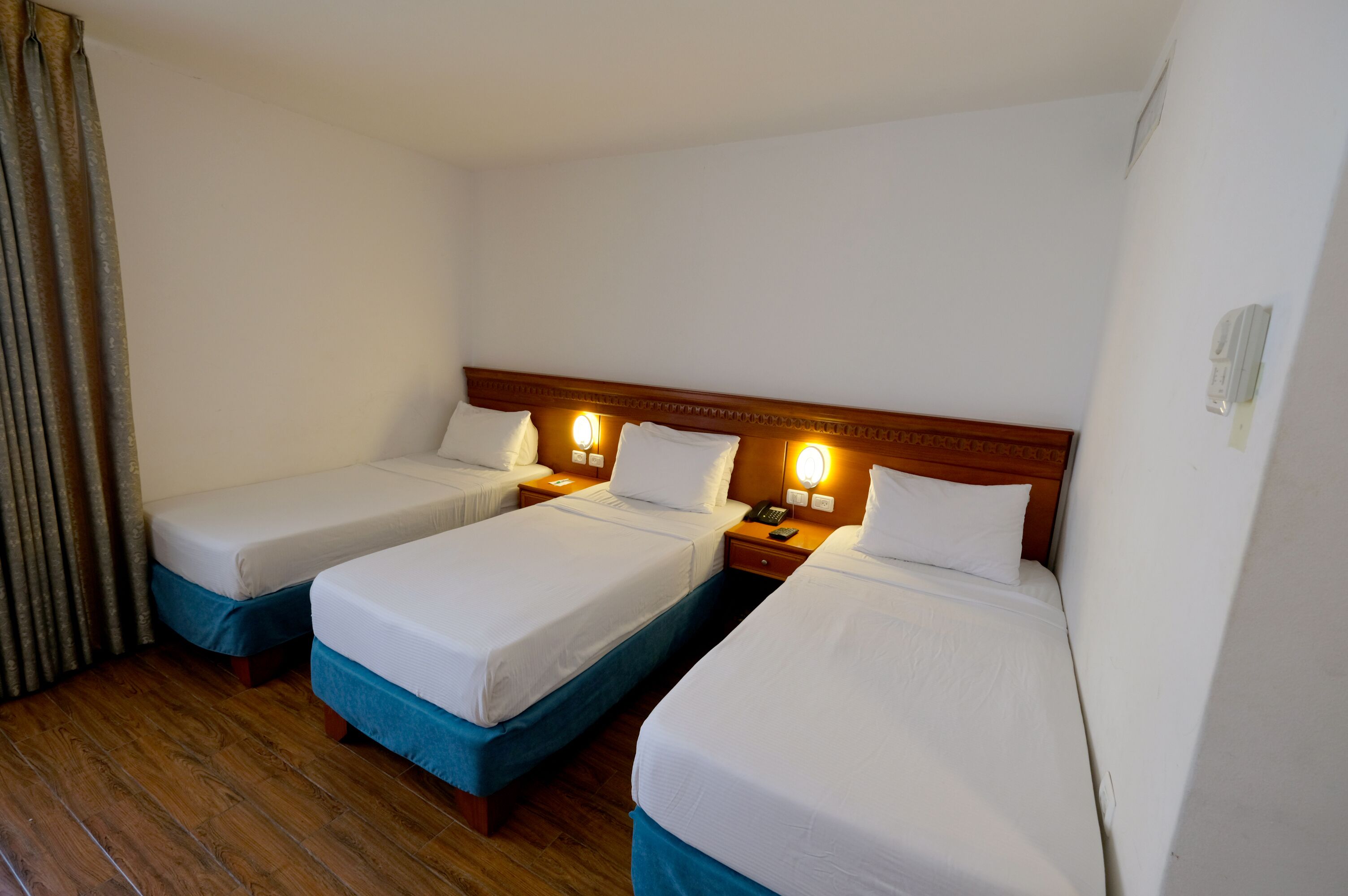 Una habitación de hotel con dos camas individuales, cabeceros de madera, lámparas de noche y suelo de madera.