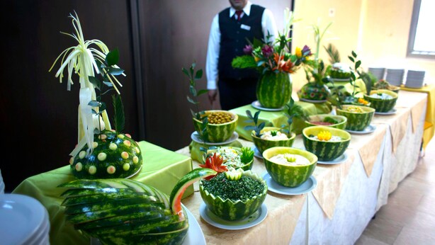 A table with creatively carved watermelon bowls, a waiter in the background, and a green tablecloth. - City Inn Palace Hotel (Ramallah)