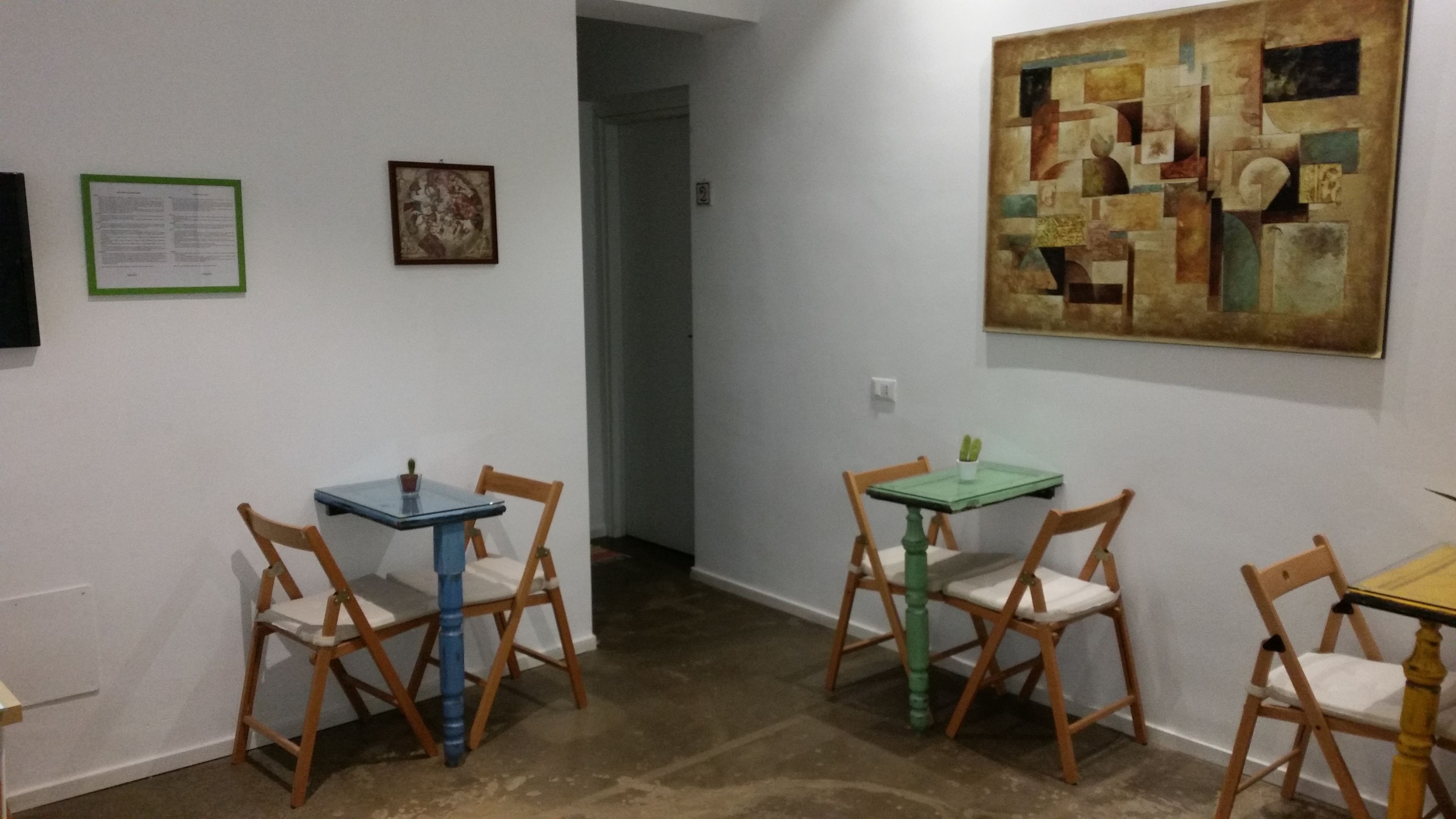 A room with two tables and four chairs, a painting on the wall, and a door leading to another room.