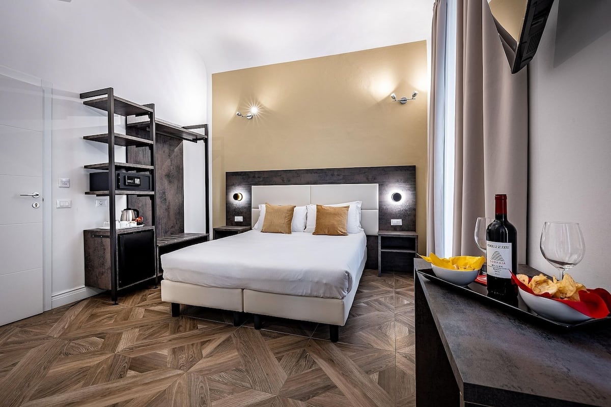 Ein modernes Hotelzimmer mit einem großen Bett, einem eingebauten Kleiderschrank, einer Minibar und einem Essbereich mit einer Weinflasche und Snacks.