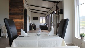 Un comedor con una mesa lista para dos personas, vista de la sala de estar y una ventana con vistas al exterior.