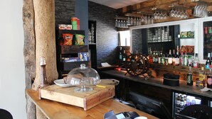 Una zona de bar con mostrador de madera, estantes con aperitivos y una exhibición de botellas, además de un espejo grande.