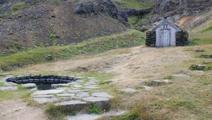 Un edificio de piedra con techo de paja, rodeado de un paisaje rocoso y un pequeño estanque.