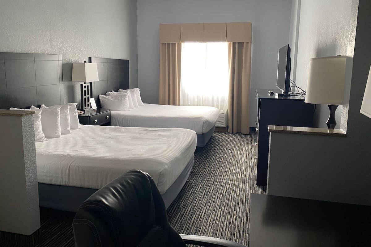 A hotel room with two beds, a desk, a chair, a TV, and a window with curtains.