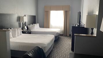 A hotel room with two beds, a desk, a chair, a TV, and a window with curtains.
