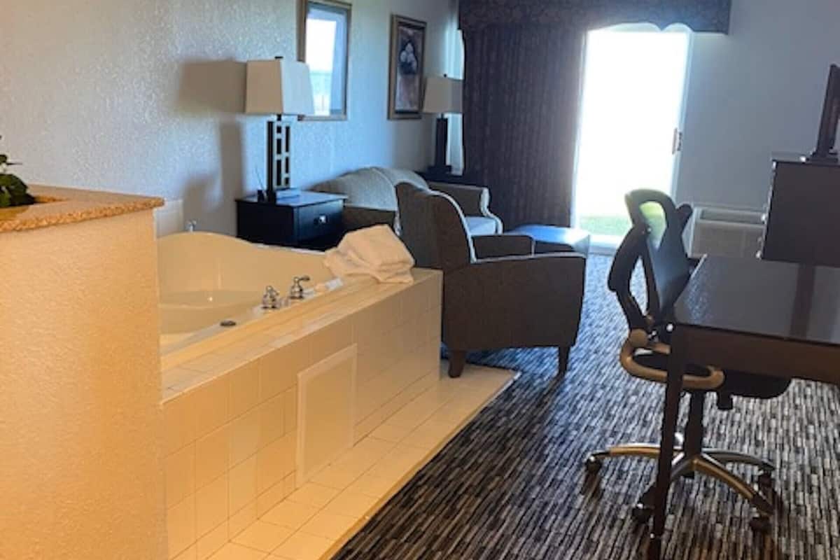 A hotel room with a large bathtub, a desk with a chair, and a television.