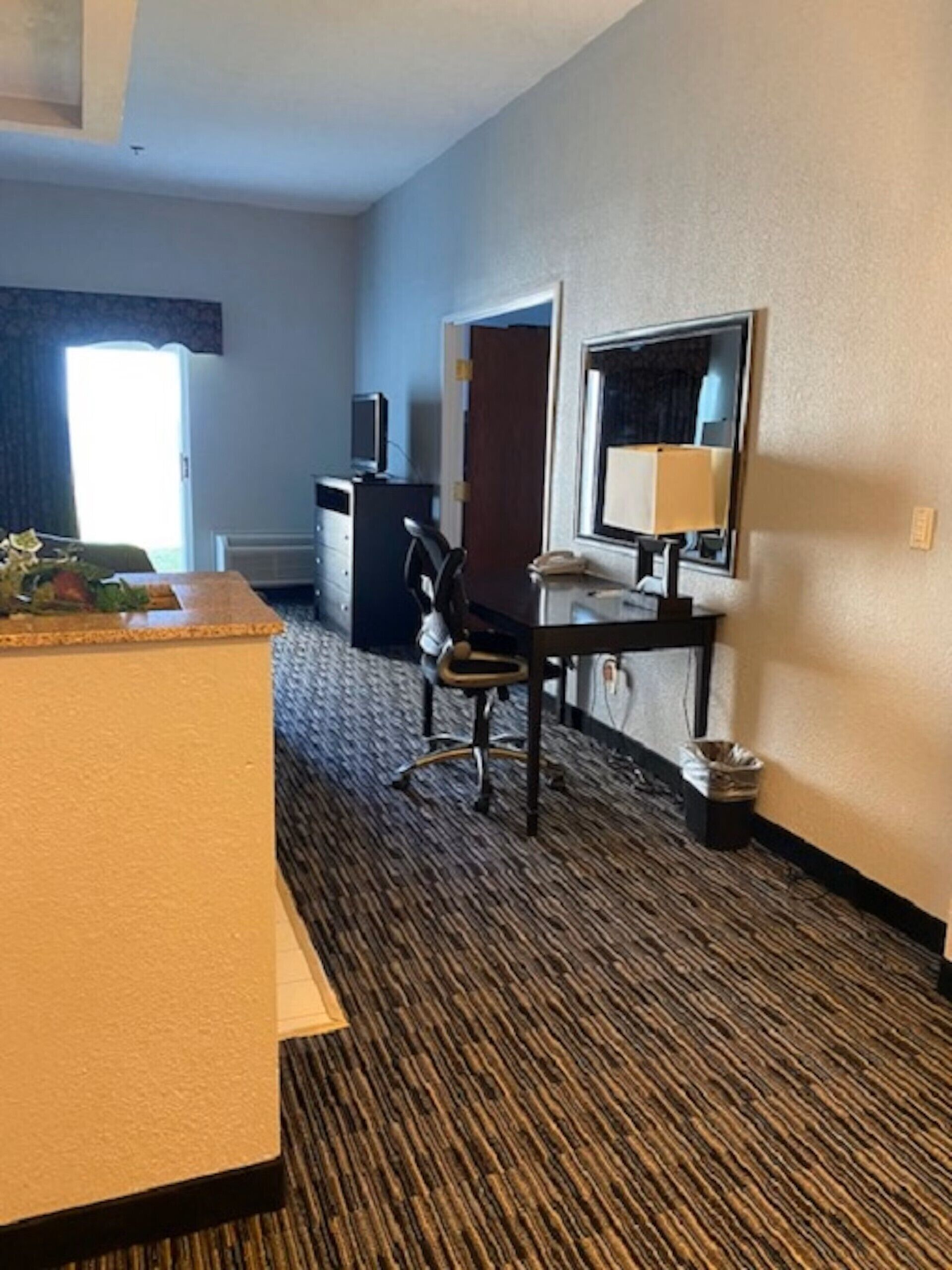 Une chambre d’hôtel avec un lit, un bureau et une chaise, une télévision et une fenêtre avec des rideaux.