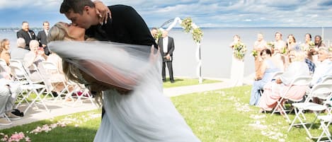 Uma cerimônia de casamento com convidados sentados em cadeiras dispostas em fileiras, olhando para o casal.