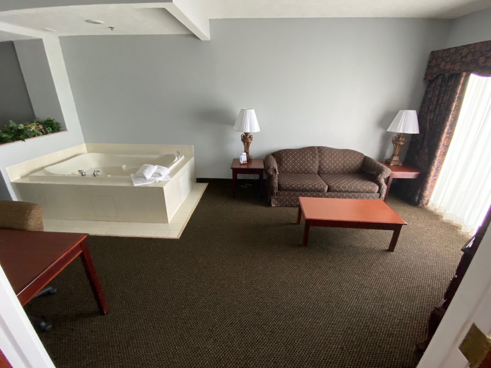 A hotel room with a large bathtub, a sofa, a small table, and two lamps.