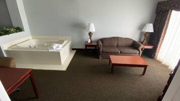 A hotel room with a large bathtub, a sofa, a small table, and two lamps.