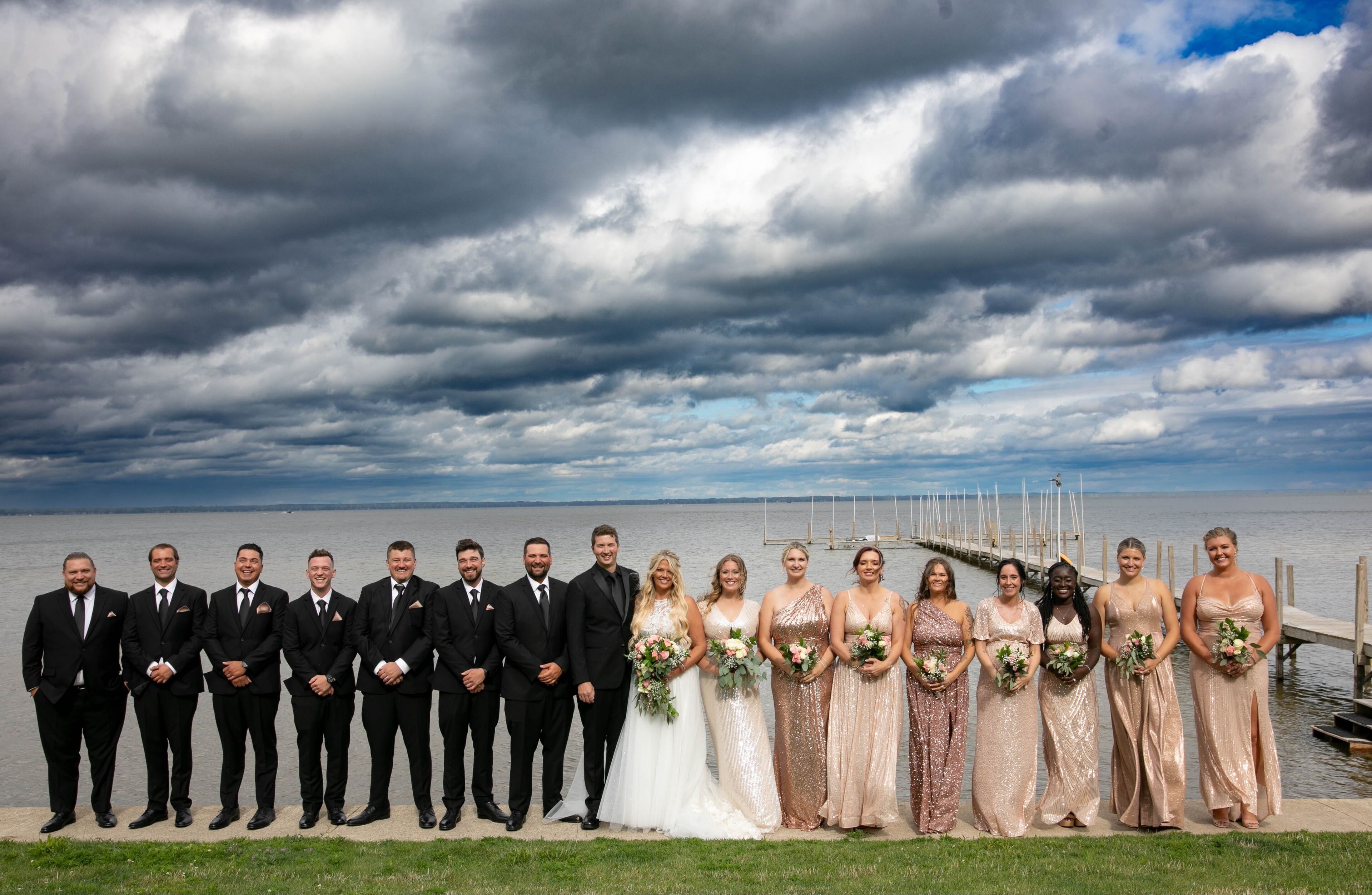A group of people standing on a dock by a body of water, with a cloudy sky in the background.