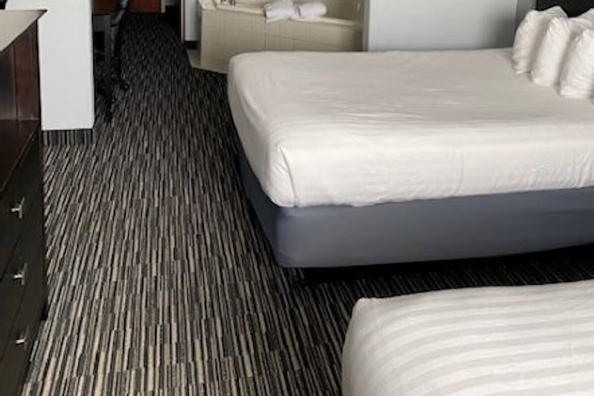 A hotel room with a large bed, a desk with a lamp, a chair, and a bathtub.