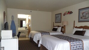 A hotel room with two beds, a desk, a refrigerator, a mirror, and a bathroom visible through an open door. - Der Ruhe Blatz Motel (Shipshewana)