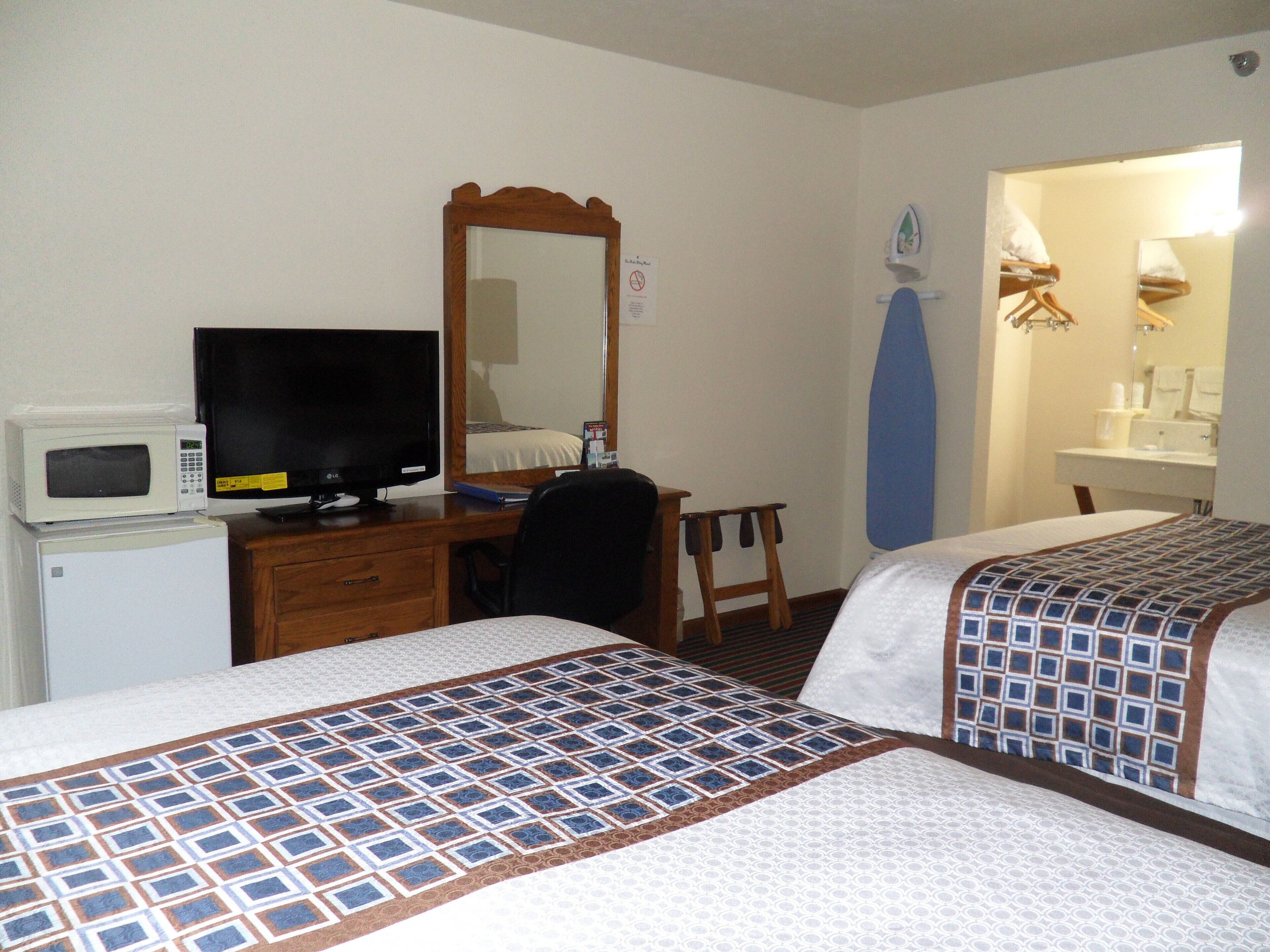 A hotel room with two beds, a desk with a computer and a TV, a microwave, and a mirror.