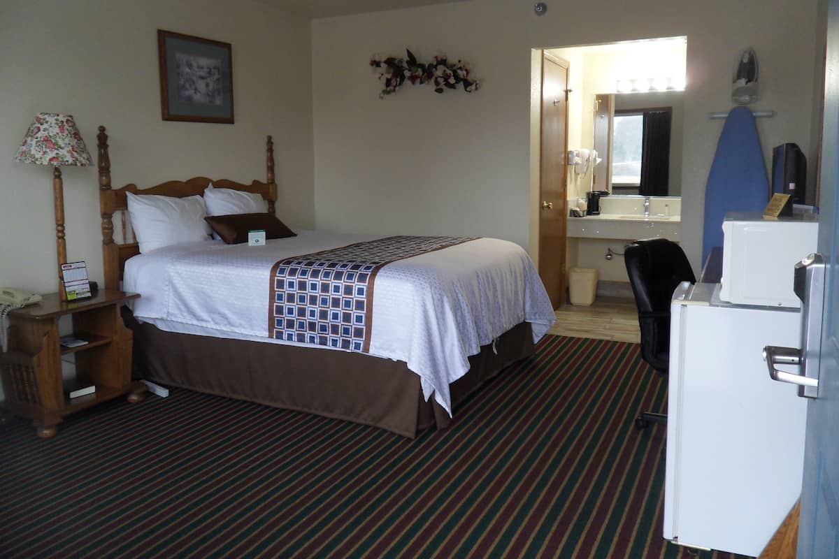 A hotel room with a bed, a desk, a chair, a refrigerator, and a bathroom visible through an open door.