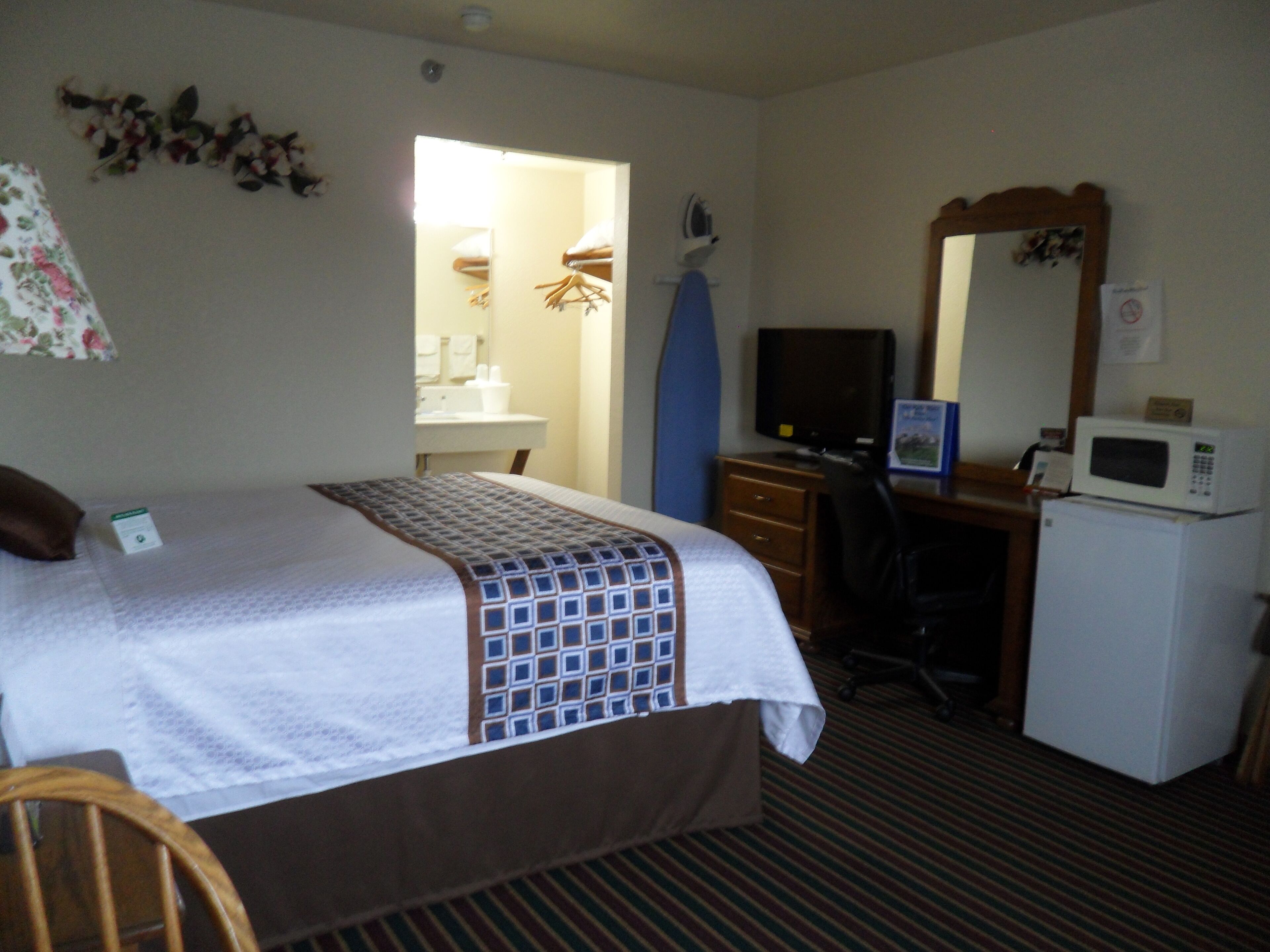 A hotel room with a bed, a desk with a computer, a microwave, and a television.