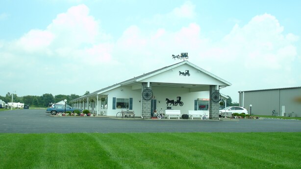 A motel with a white exterior, a covered front porch, and a horse-drawn carriage decoration. - Der Ruhe Blatz Motel (Shipshewana)