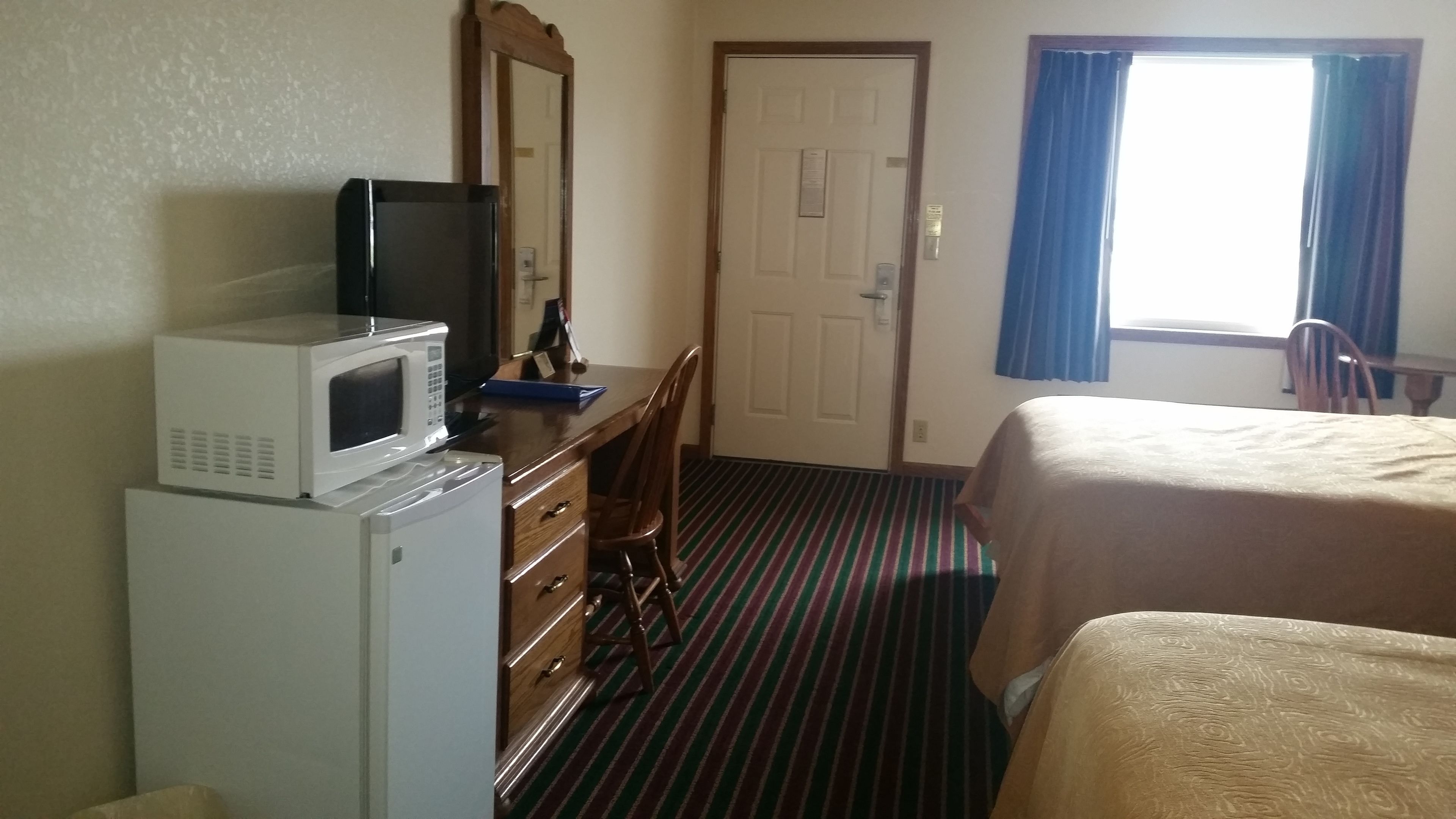 Una habitación de hotel con una cama, un escritorio con microondas, una silla y una puerta.