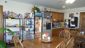 A dining area with a wooden table and chairs, surrounded by shelves stocked with snacks and beverages. - Der Ruhe Blatz Motel (Shipshewana)