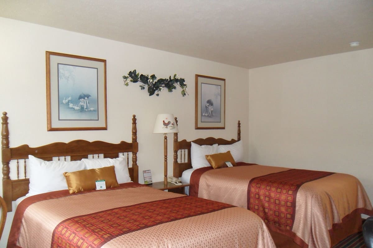A hotel room with two beds, each with a wooden headboard, white and brown bedding, and framed pictures on the walls.