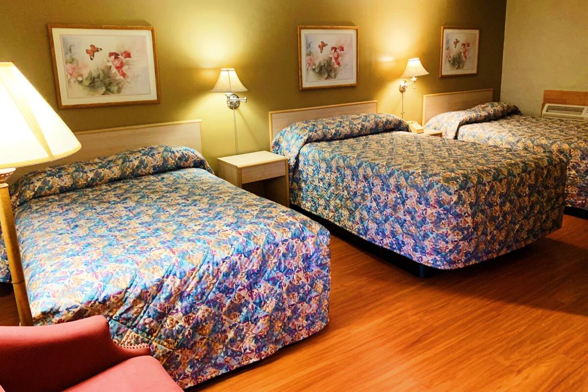 A hotel room with two beds, floral-patterned bedding, bedside lamps, and floral artwork on the walls.