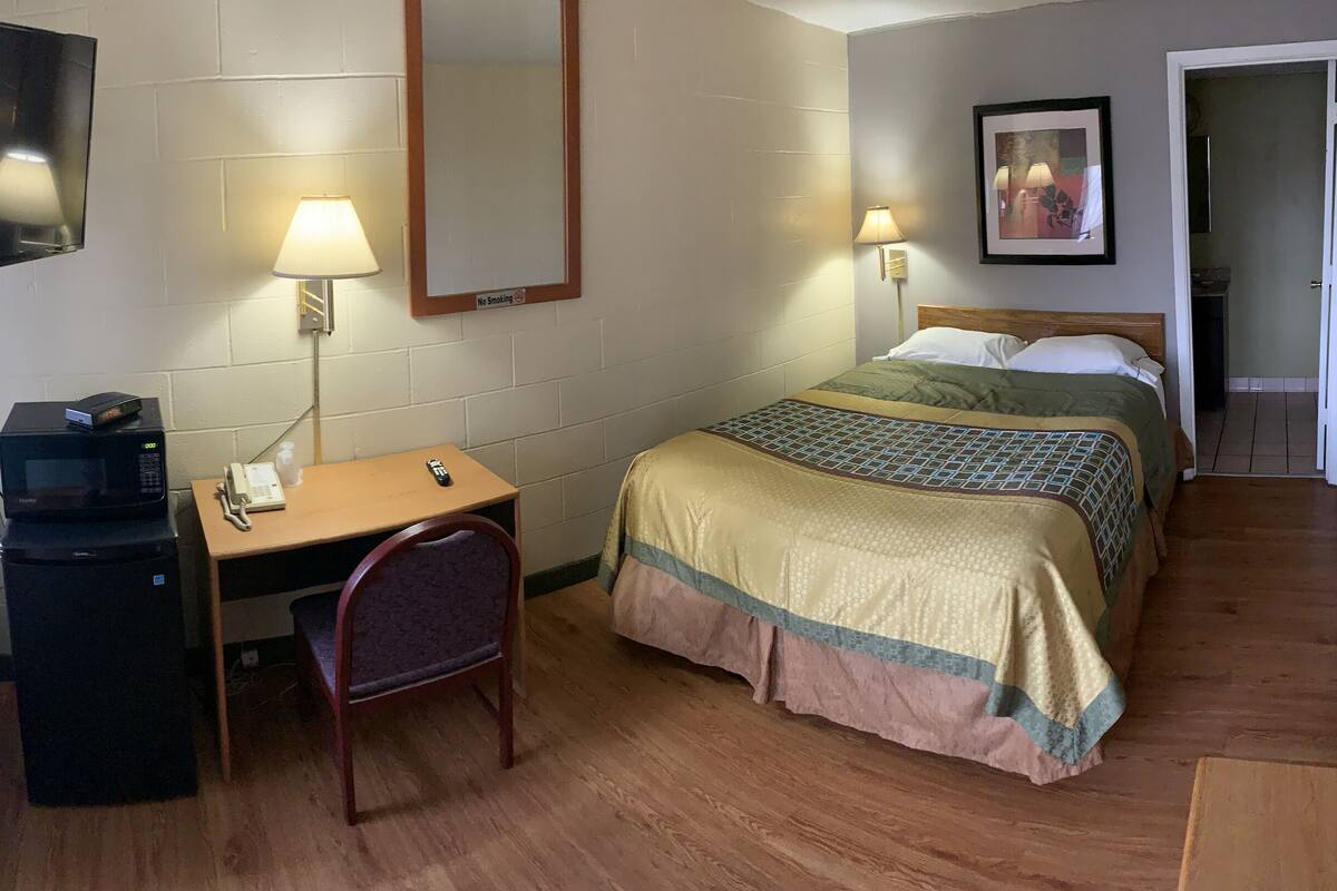 A hotel room with a desk, chair, two beds, a TV, and a mirror.